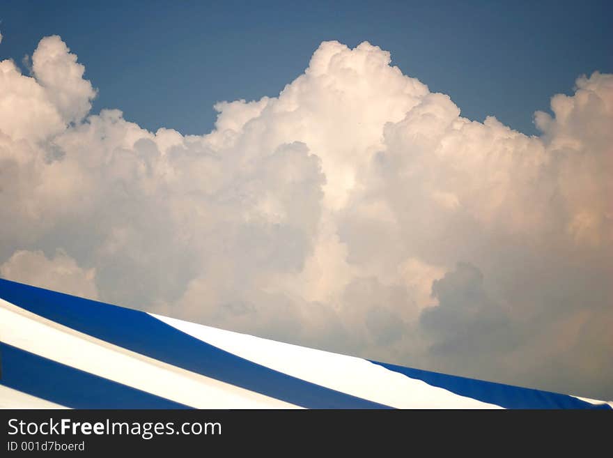 A blue and white stripped roof abstract against a blue and cotton candy clouds.