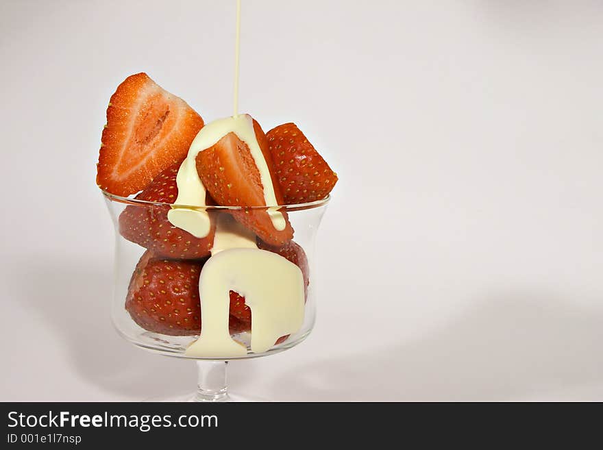 Pouring cream over a dessert glass full of ripe juicey strewberries. Pouring cream over a dessert glass full of ripe juicey strewberries.