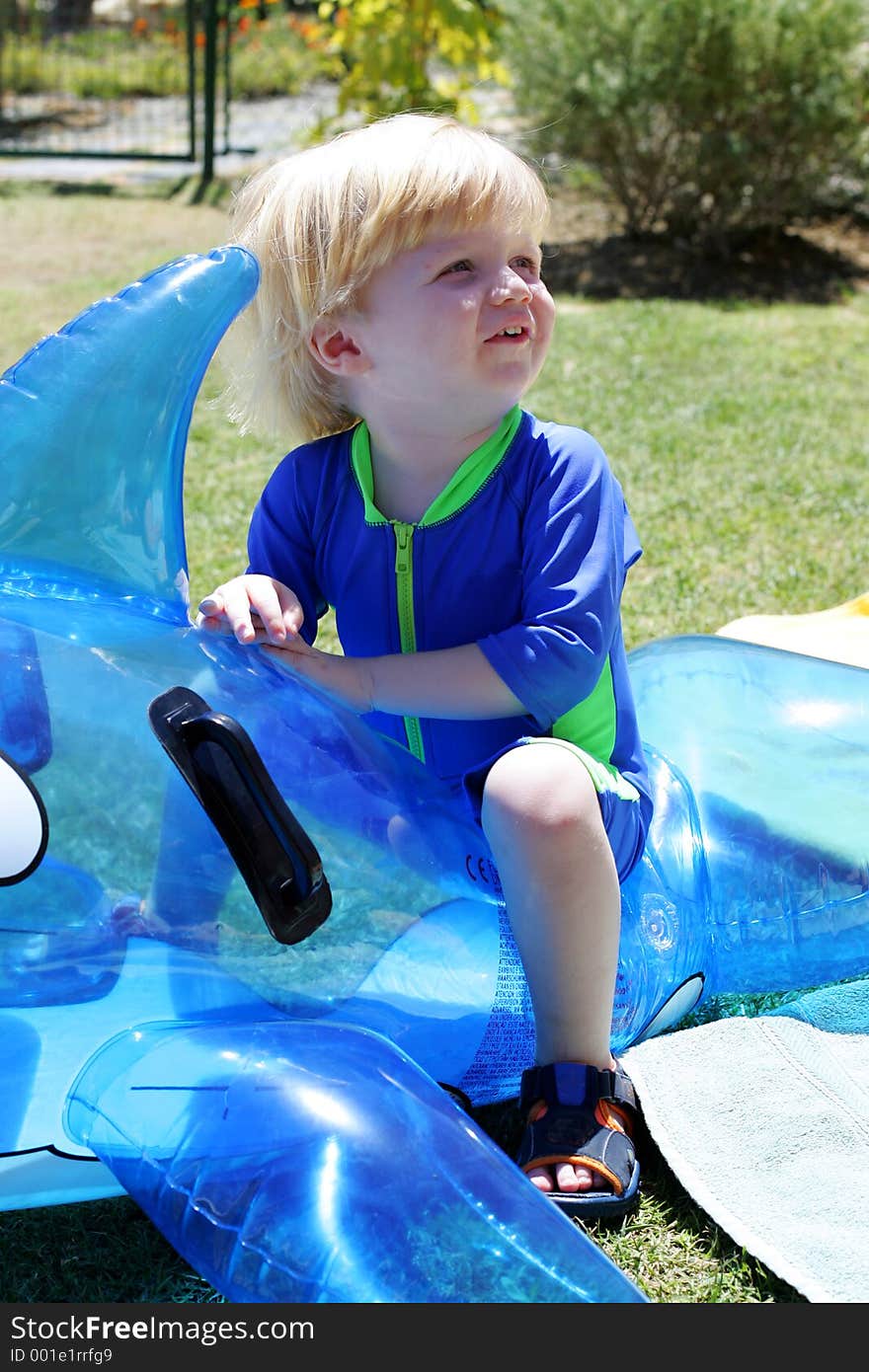 Young boy or child sitting on inflatable dolphin by swimming pool