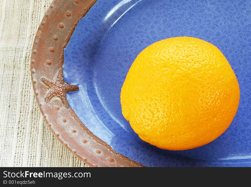 Ripe orange in blue dish with sea motif. Ripe orange in blue dish with sea motif