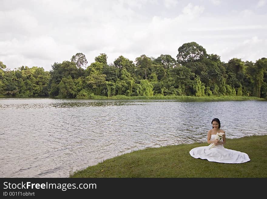 A beautiful asian woman in her wedding dress sits by the side of a lake in Singapore. A beautiful asian woman in her wedding dress sits by the side of a lake in Singapore