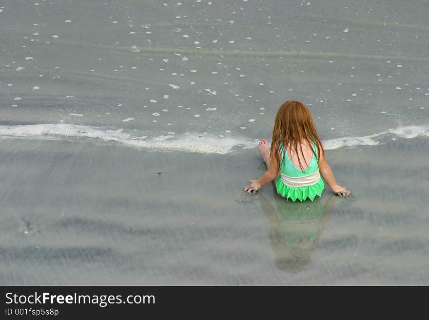 Little girl in green bathing suite on the beach, playing in the sand. Little girl in green bathing suite on the beach, playing in the sand.