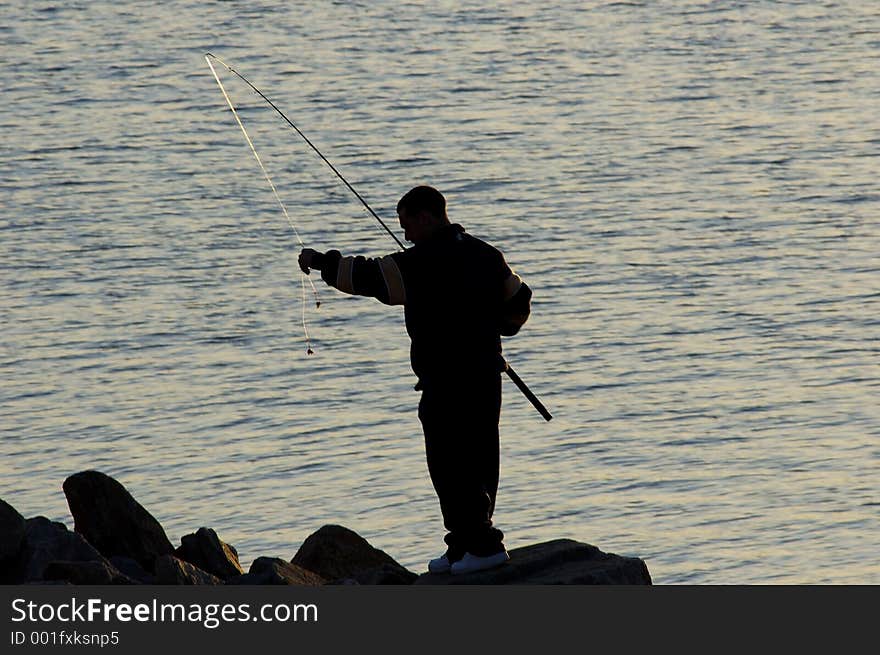 A silhouette of a man preparing to cast his fishing line as the sun goes down. A silhouette of a man preparing to cast his fishing line as the sun goes down.