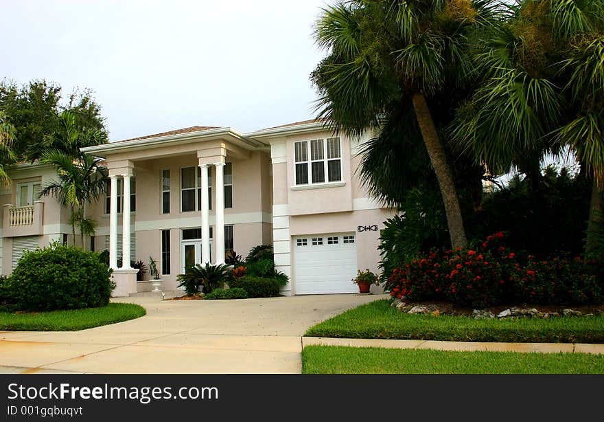 Beautiful home in tropics, with two sets of double columns and a wide driveway leading to front door, surrounded by tropical landscaping