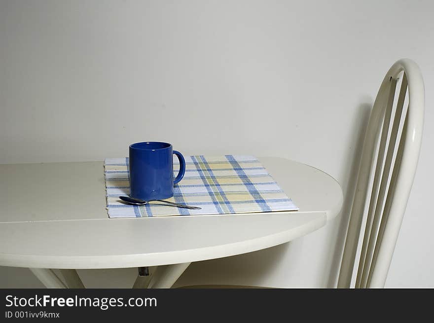A coffee mug sitting on a table, with an empty chair. A coffee mug sitting on a table, with an empty chair