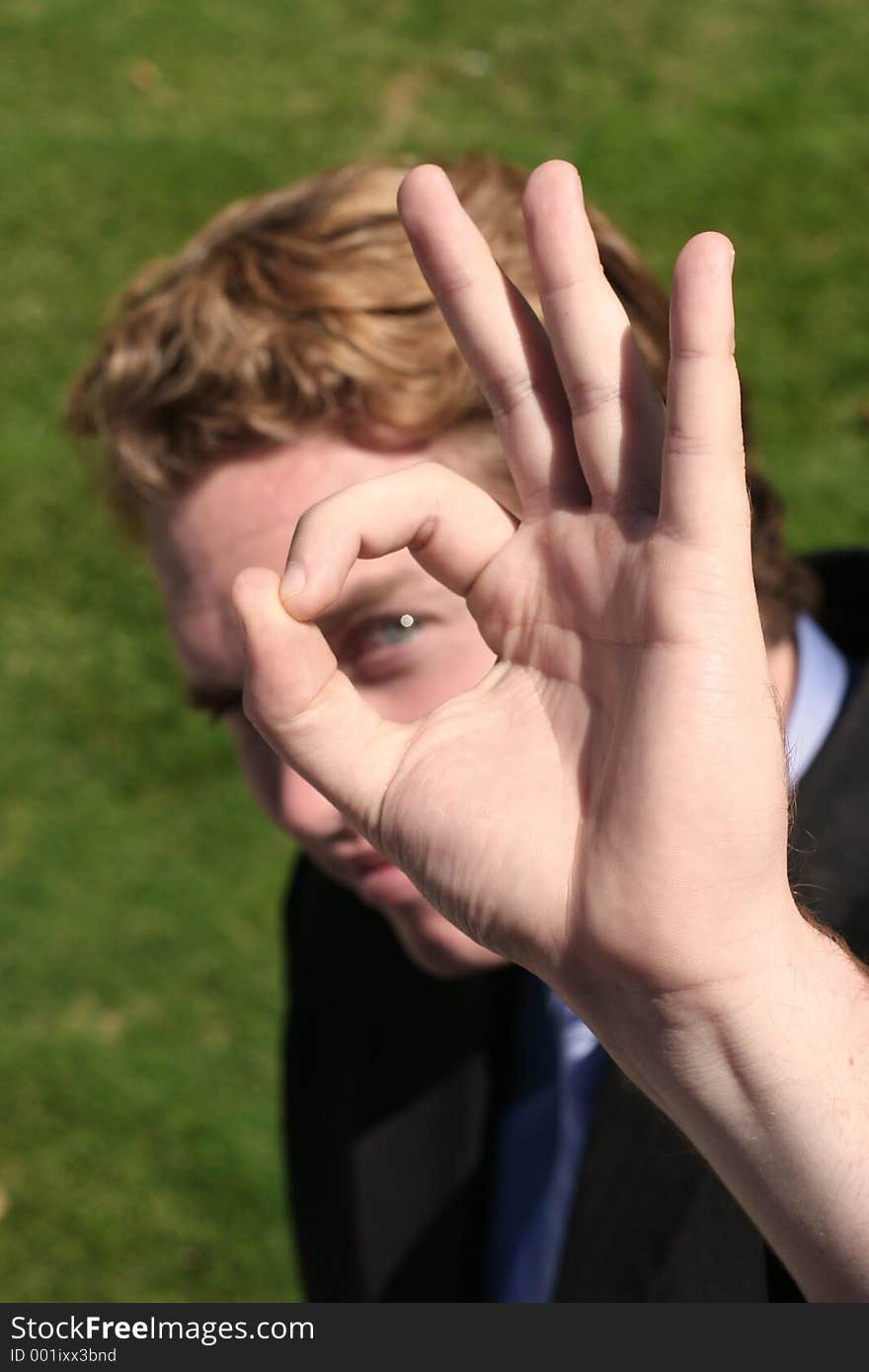 Through the OK sign, a businessman's eye can be seen, with green grass background. Through the OK sign, a businessman's eye can be seen, with green grass background