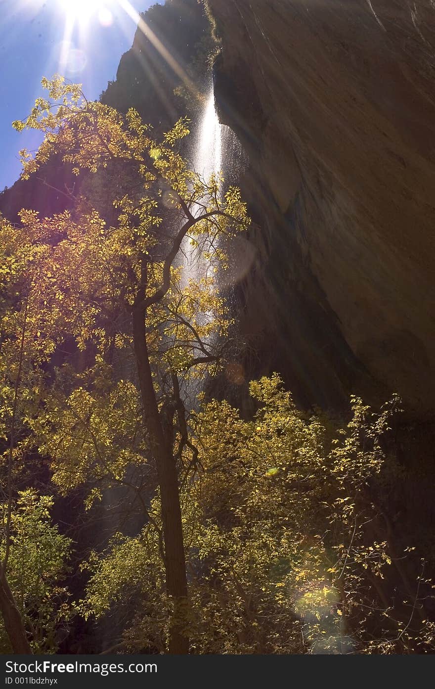 A waterfall in the middle of a canyon, with the sun shining bright up above. A waterfall in the middle of a canyon, with the sun shining bright up above