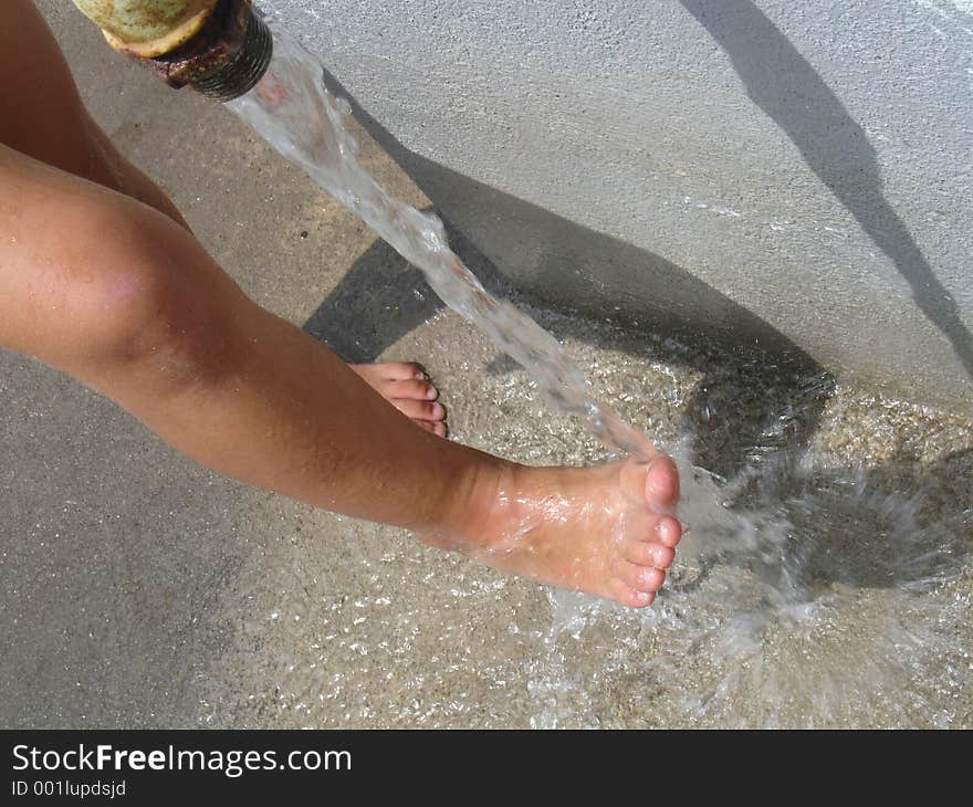 Child is rinsing her feet in cold water form teh well. Child is rinsing her feet in cold water form teh well