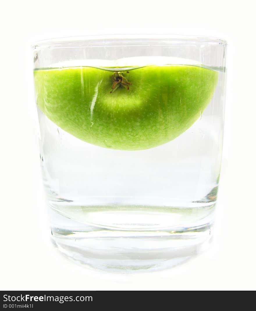 Half a green apple floating in a glass of water. Half a green apple floating in a glass of water