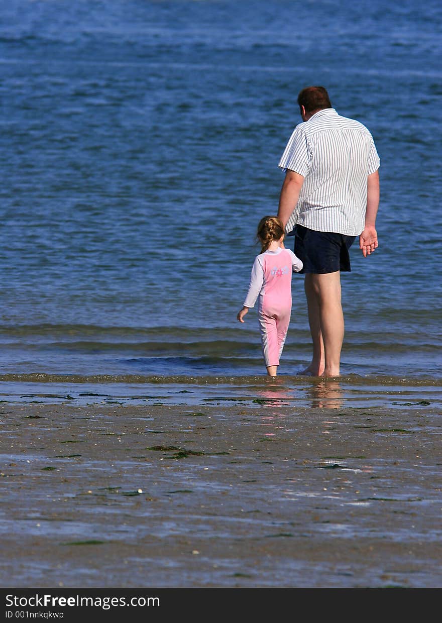 A father holding the hand of his daughter at the beach, whilst paddling together. A father holding the hand of his daughter at the beach, whilst paddling together.