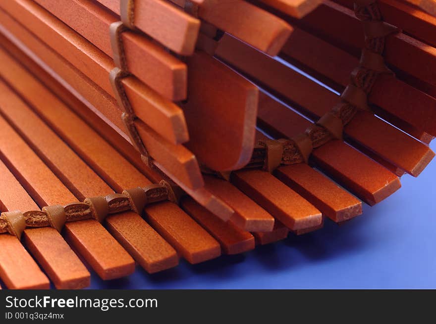 A partially rolled up wooden place mat on a smooth blue background. -- Controlled depth of field. A partially rolled up wooden place mat on a smooth blue background. -- Controlled depth of field