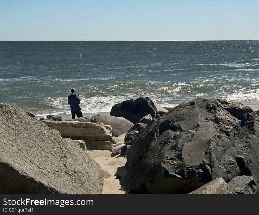 A man fishing along a rocky shoreline at Sandy Hook, NJ. A man fishing along a rocky shoreline at Sandy Hook, NJ.