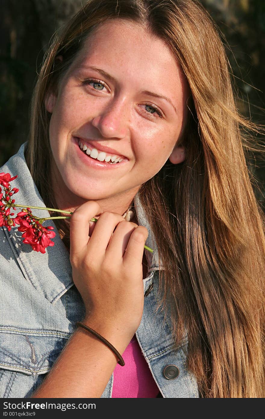 A beautiful teen-aged girl smiling and holding a flower. A beautiful teen-aged girl smiling and holding a flower.