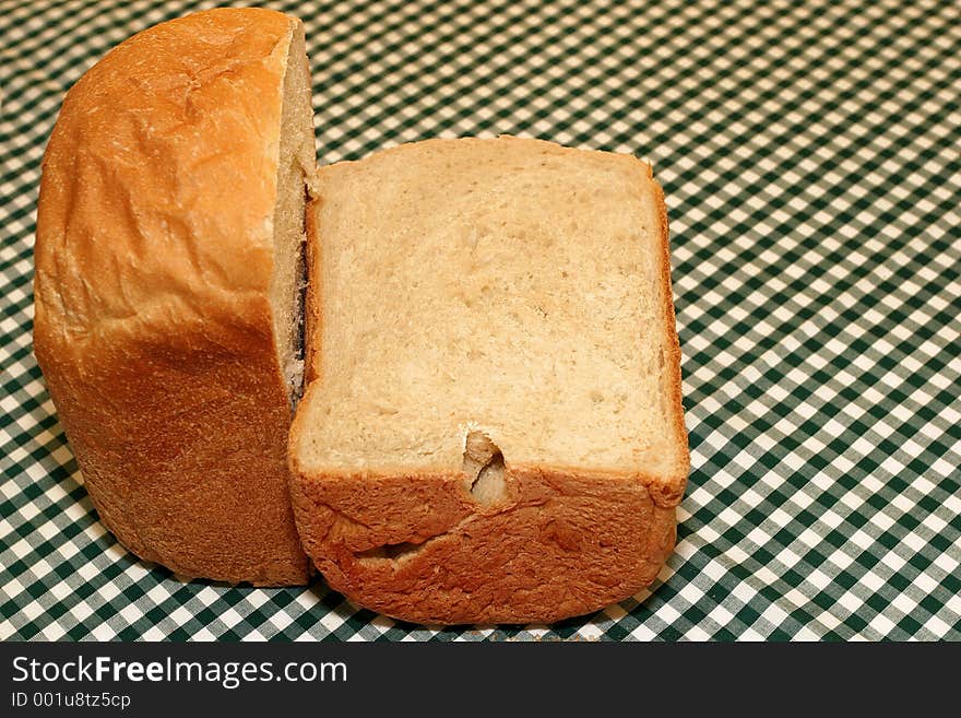 A loaf of freshly baked bread cut in half on a geen and white chequered cloth. A loaf of freshly baked bread cut in half on a geen and white chequered cloth.