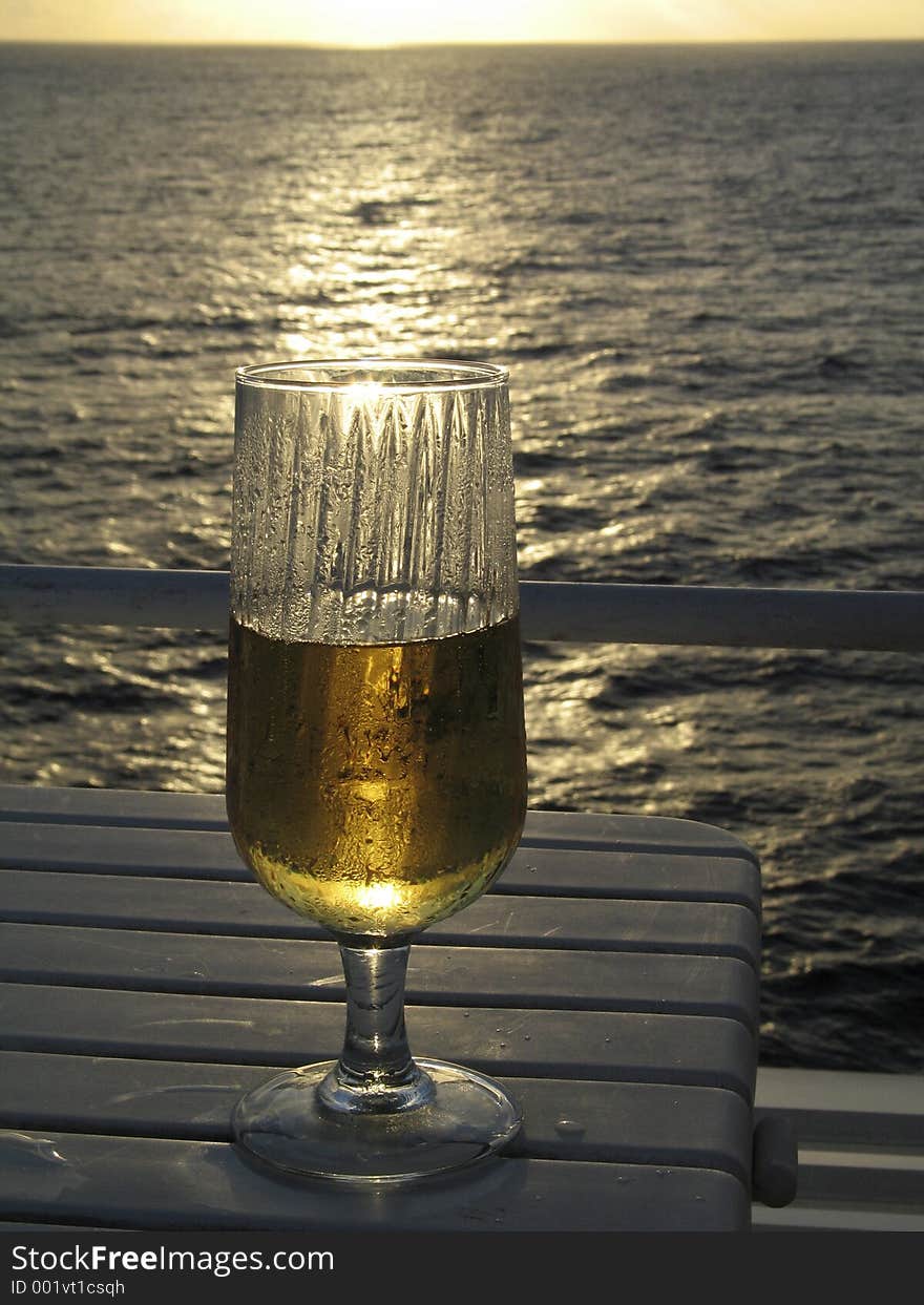 Glass of Beer illuminated by the sunset with the ocean in the background. Glass of Beer illuminated by the sunset with the ocean in the background