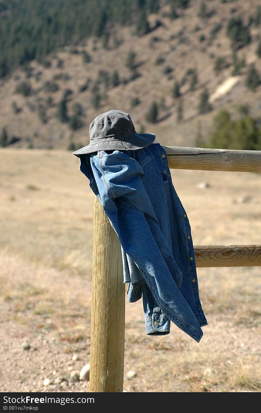 Coat and hat have been left on a fence post in the mountains. Coat and hat have been left on a fence post in the mountains