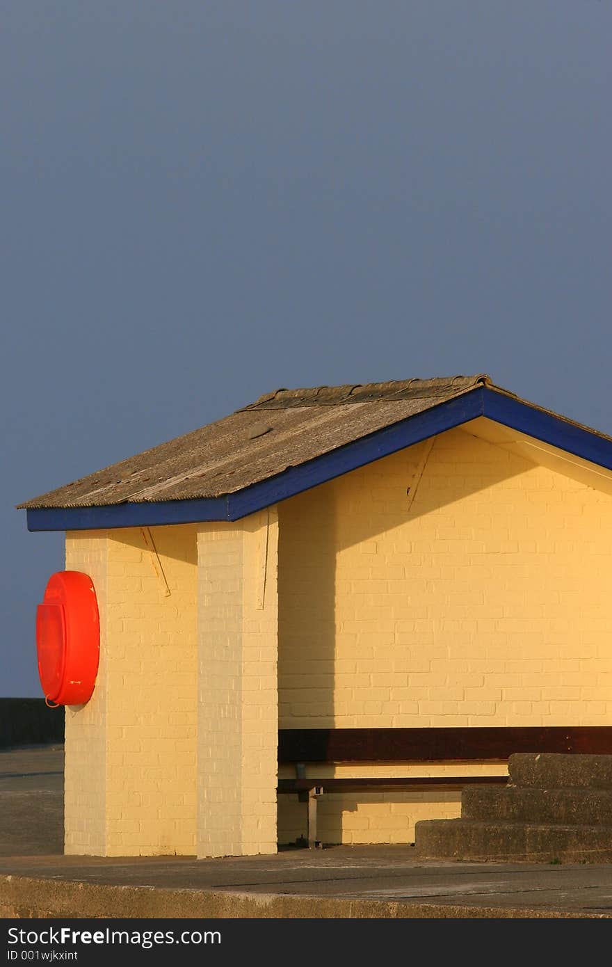 Brick shelter on a promenade, painted yellow and blue, with a bright orange, lifebuoy attached to the side. Brick shelter on a promenade, painted yellow and blue, with a bright orange, lifebuoy attached to the side.
