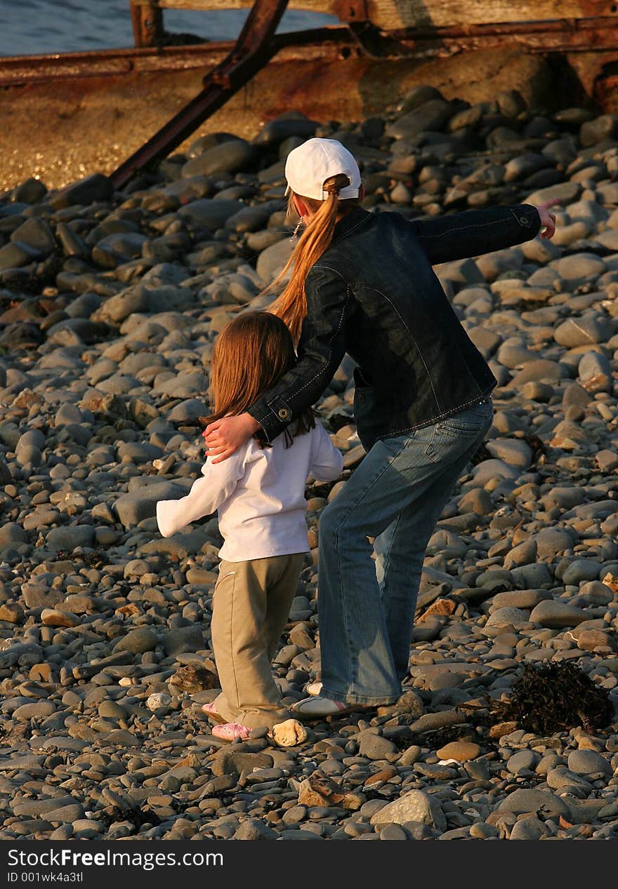 A young girl with her arm protectively around a younger child, standing on a pebble beach. A young girl with her arm protectively around a younger child, standing on a pebble beach.