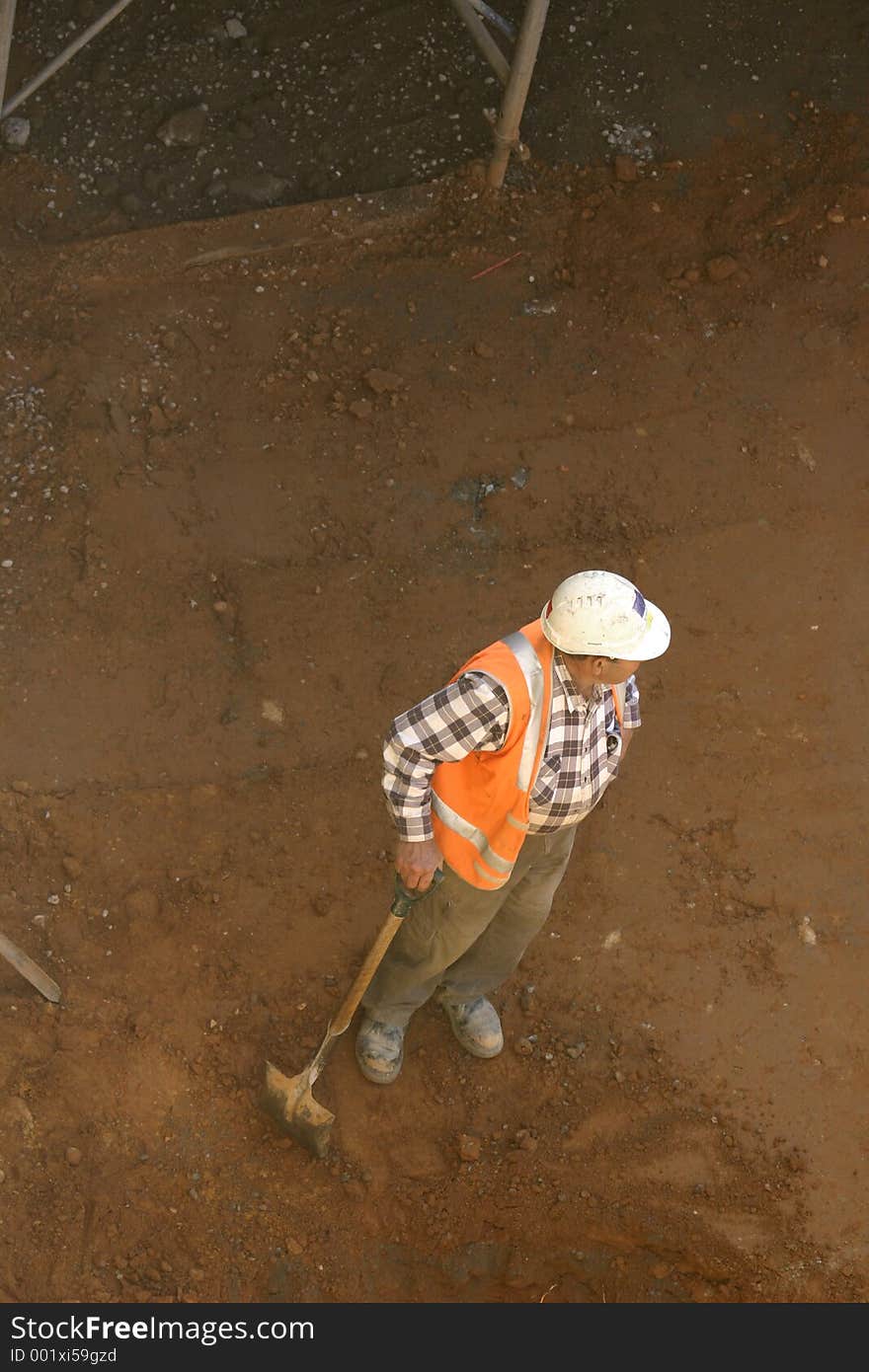 A workman leans on his shovel in a dirt pit. A workman leans on his shovel in a dirt pit