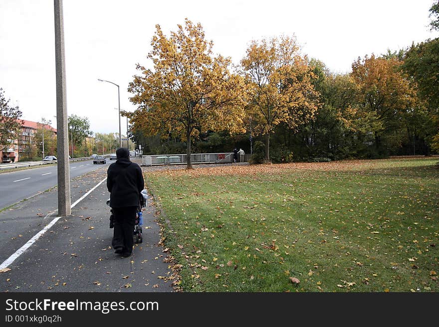 Lady pushing a pram through roadside in autumn. Lady pushing a pram through roadside in autumn.