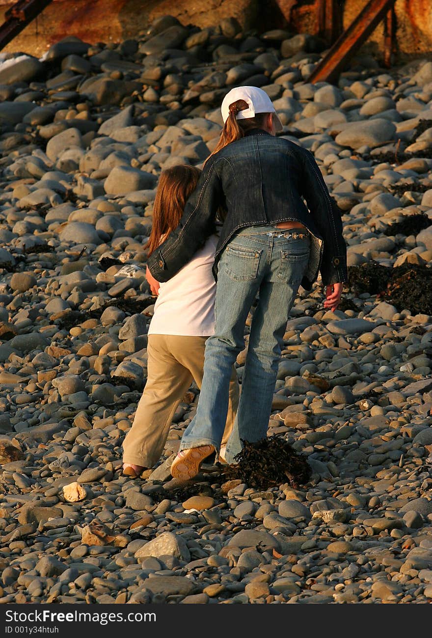 A young girl standing on a pebble beach, with her arm protectively around a younger child,