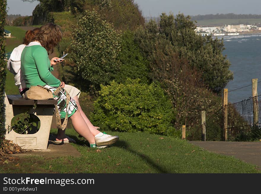 Girls Sitting On Bench Overlooking Sea