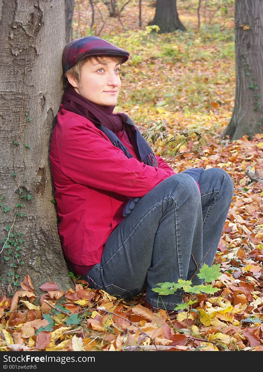 Model in vizored cap and muffler sitting by the tree. Model in vizored cap and muffler sitting by the tree