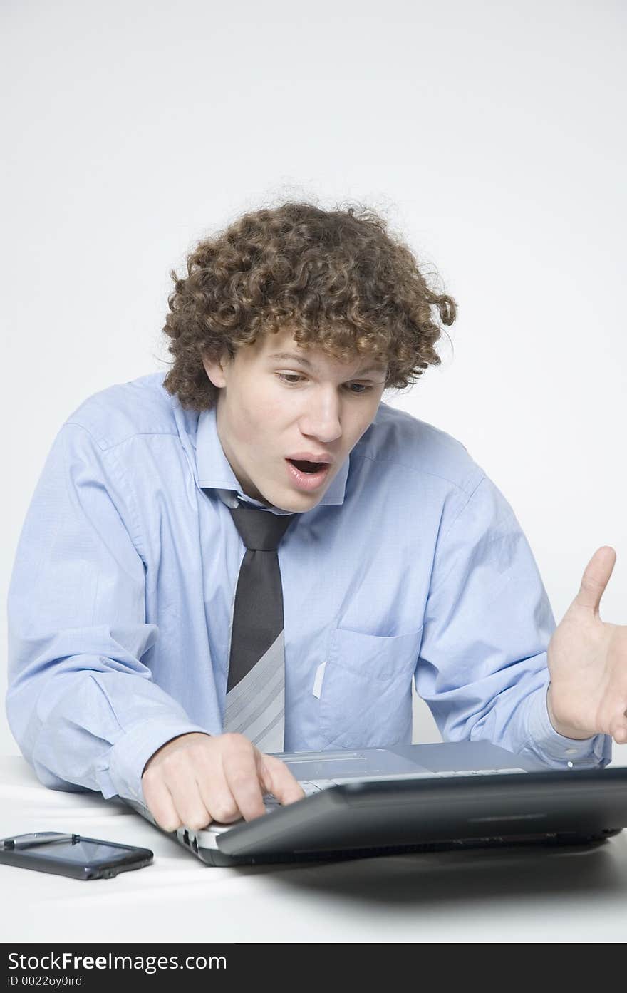 (Boy in relaxed office attire) Boy sitting at a table with a laptop and palm is looking at the laptop with a surprised expression. (Boy in relaxed office attire) Boy sitting at a table with a laptop and palm is looking at the laptop with a surprised expression