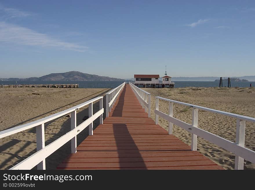 A boardwalk leads across the sand to a small boathouse at the end of a pier.