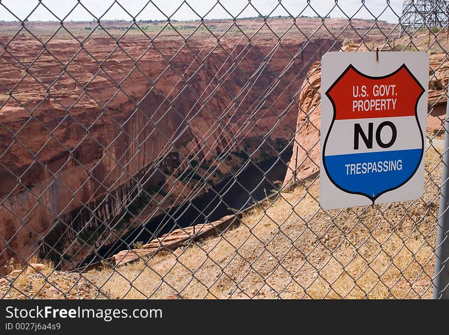 A bright red, white and blue sign on a chain link fence keeps citizens out of scenic red sandstone canyons and the cliffs near Glen Canyon Dam in Arizona. A bright red, white and blue sign on a chain link fence keeps citizens out of scenic red sandstone canyons and the cliffs near Glen Canyon Dam in Arizona