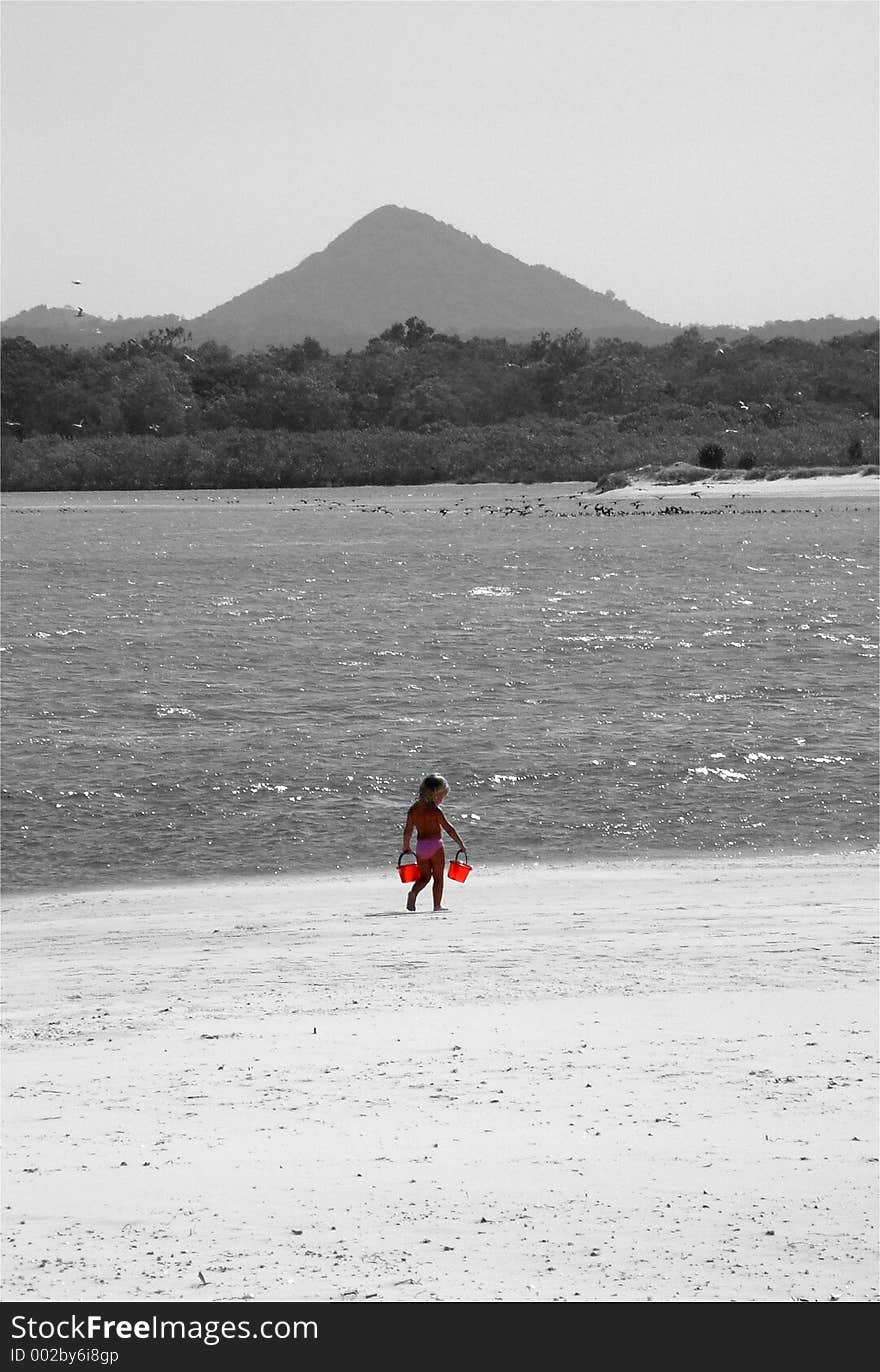 A little girl strolls along the beach with her red buckets