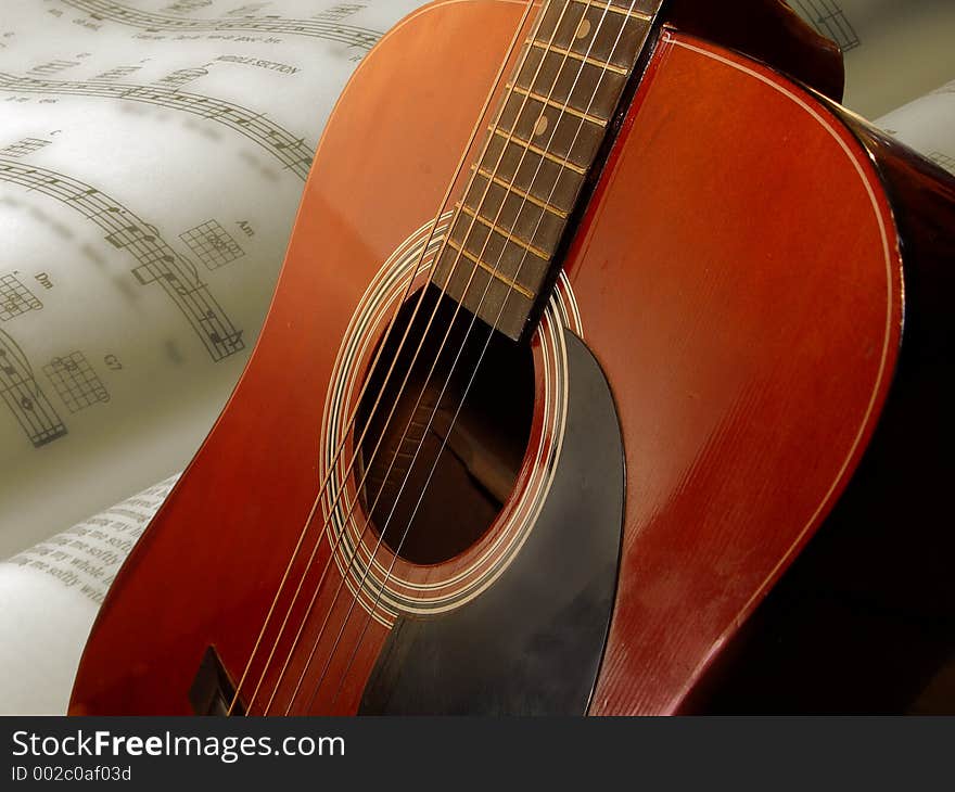 Acoustical guitar standing with an opened page of sheetmusic in the background. Acoustical guitar standing with an opened page of sheetmusic in the background.