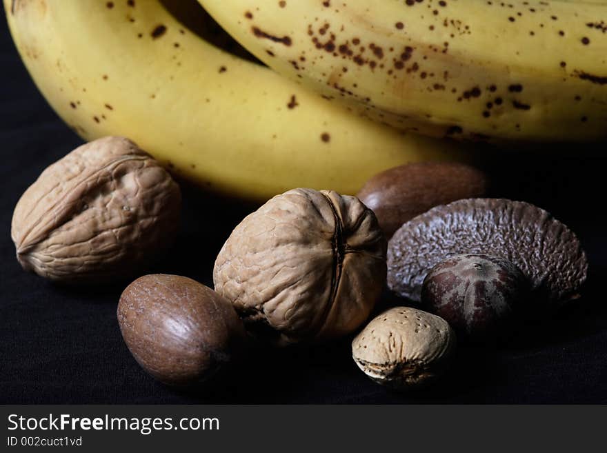 Mixed nuts beside bananas up close on black background