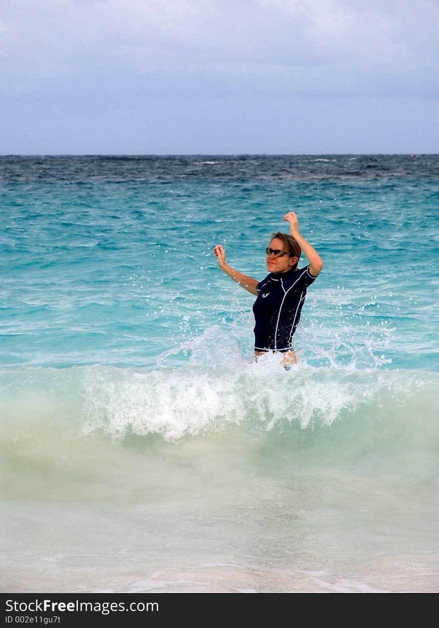 A blonde girl splashes in the waves of a green ocean. A blonde girl splashes in the waves of a green ocean.