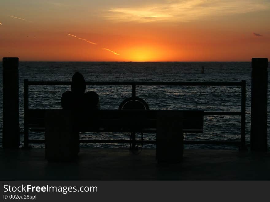 Man sitting on bench at pier at sun set. Man sitting on bench at pier at sun set