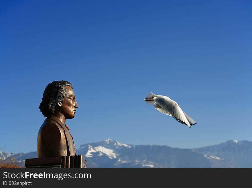 A seagull fly from the top of the statue and it seem that the statue looks the bird