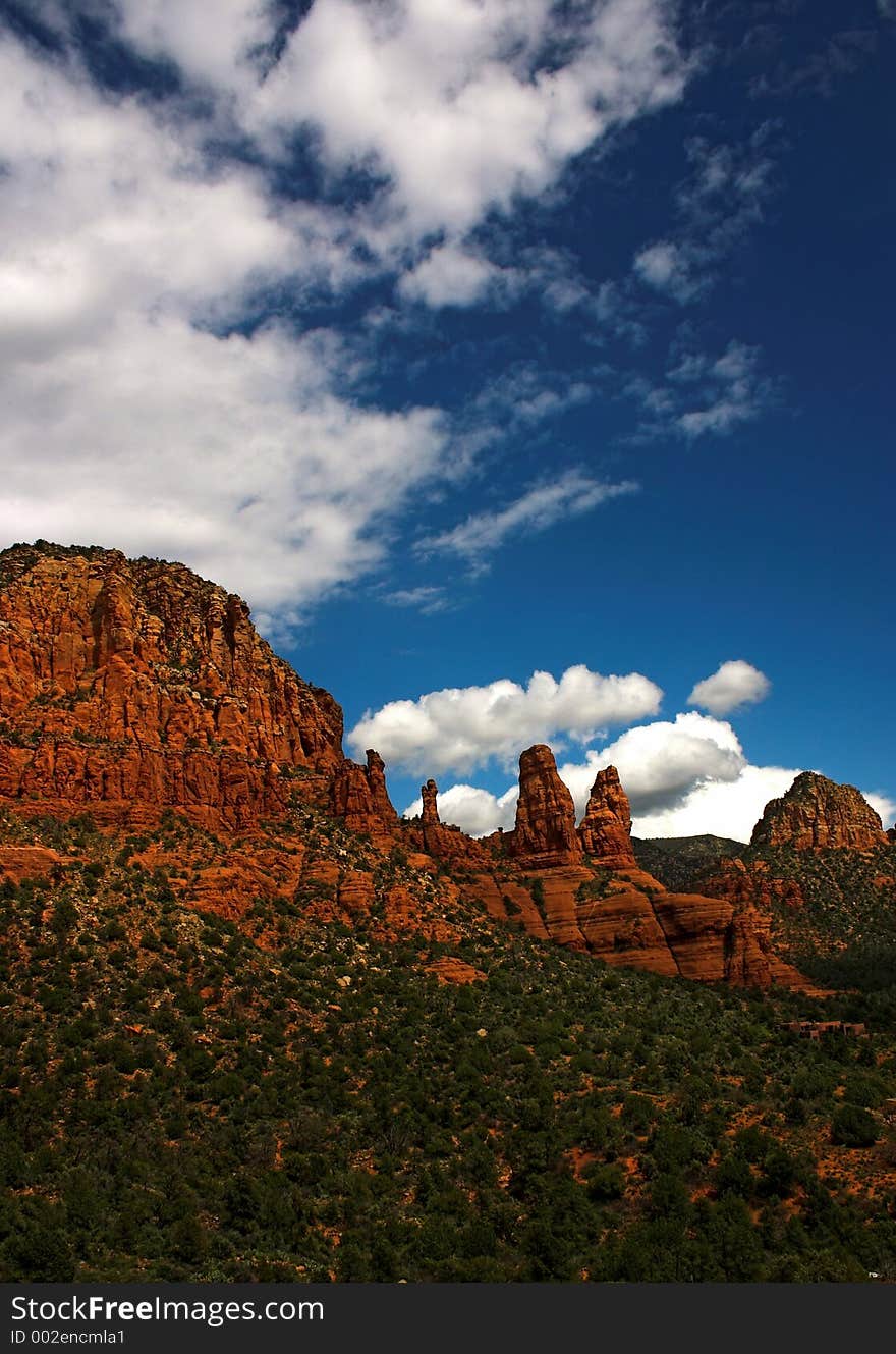 Some cliffs in the foreground against a blue sky with some clouds. The desert is quite green because of recent rain that caused growth in the summer. This location is near Sedona a very popular vacation spot. Some cliffs in the foreground against a blue sky with some clouds. The desert is quite green because of recent rain that caused growth in the summer. This location is near Sedona a very popular vacation spot.