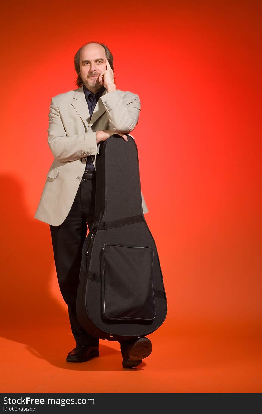 Middle aged man-musician with his guitar carrying case on a red background.