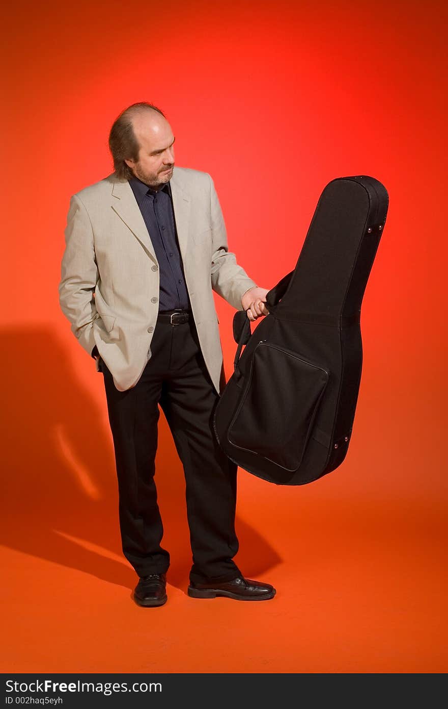 Middle aged thoughtful man-musician with his guitar carrying case on a red background. Middle aged thoughtful man-musician with his guitar carrying case on a red background.