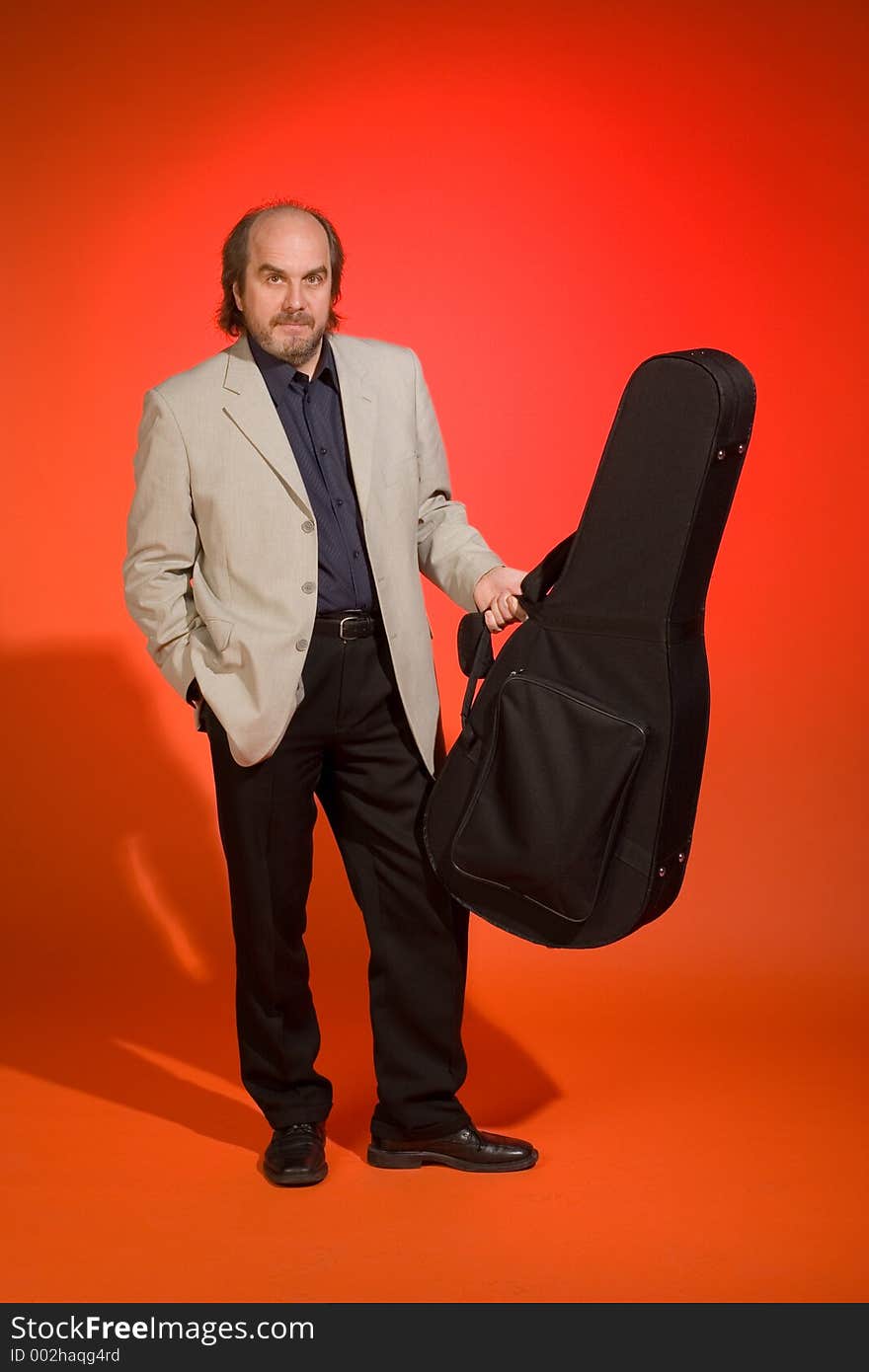 A Proud looking middle aged man-musician with his guitar carrying case on a red background. A Proud looking middle aged man-musician with his guitar carrying case on a red background.