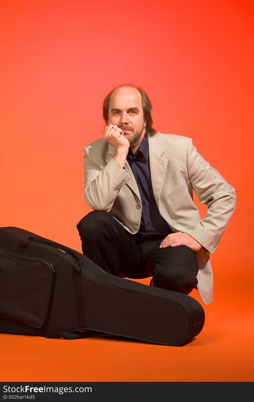 Middle aged thoughtful man-musician with his guitar carrying case on a red background. Middle aged thoughtful man-musician with his guitar carrying case on a red background.