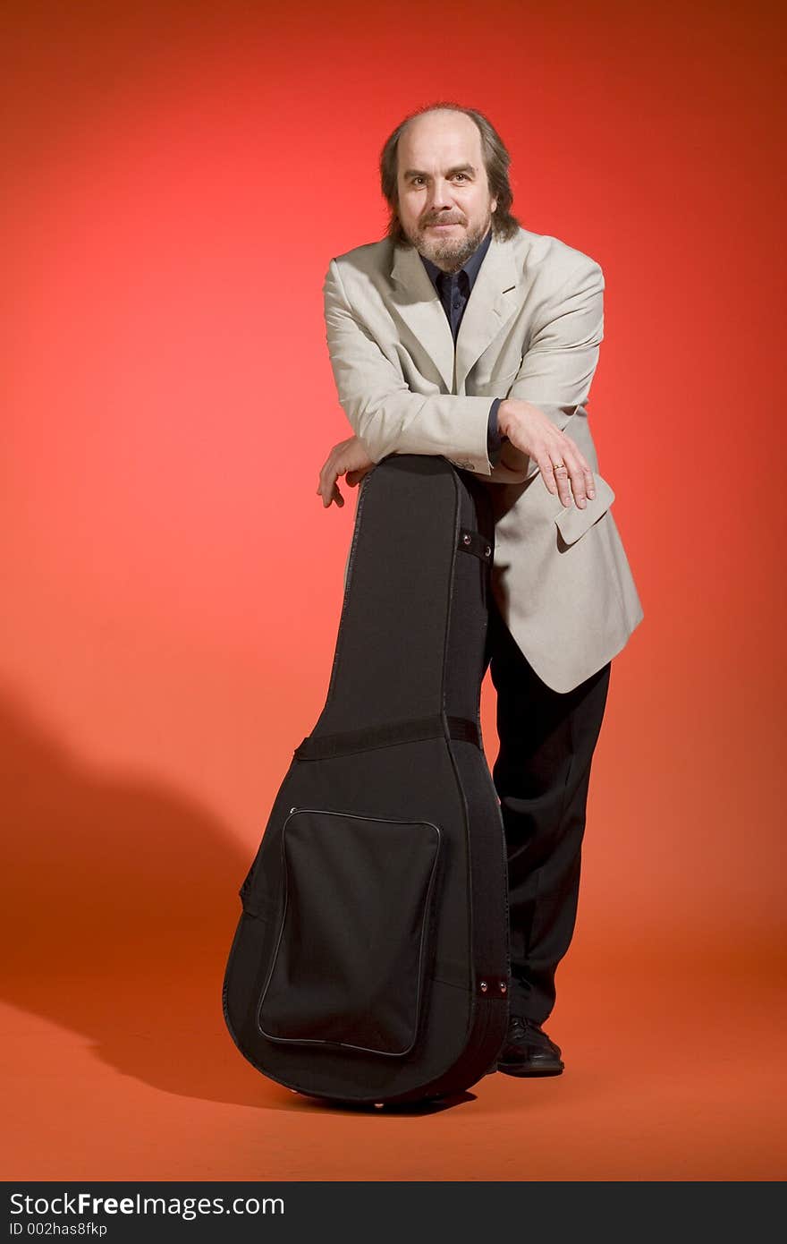 A happy looking middle aged man-musician with his guitar carrying case on a red background. A happy looking middle aged man-musician with his guitar carrying case on a red background.