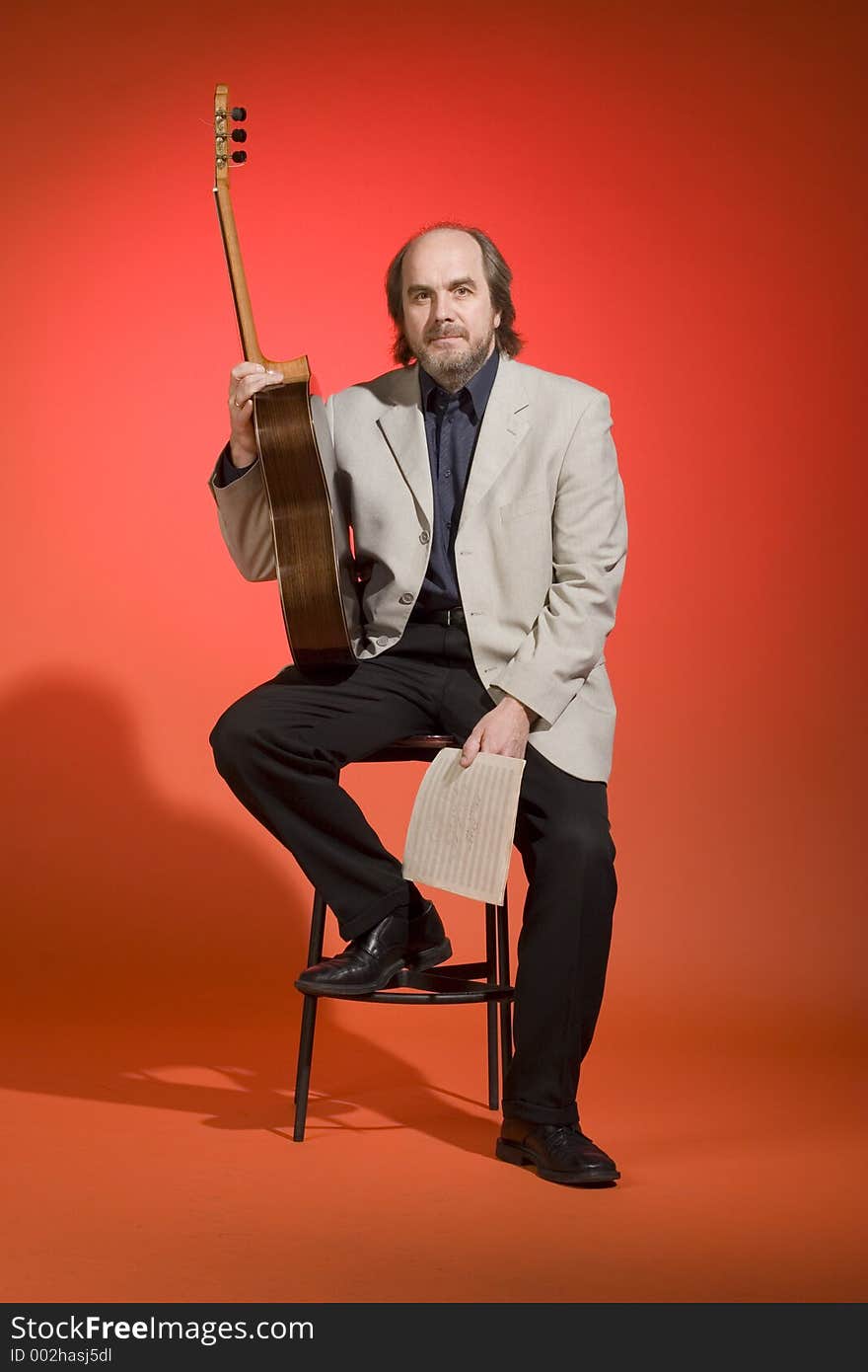 Middle aged man-musician leaning on a chair with his guitar and musical notes in his hands on a red background. Last of the series! :)