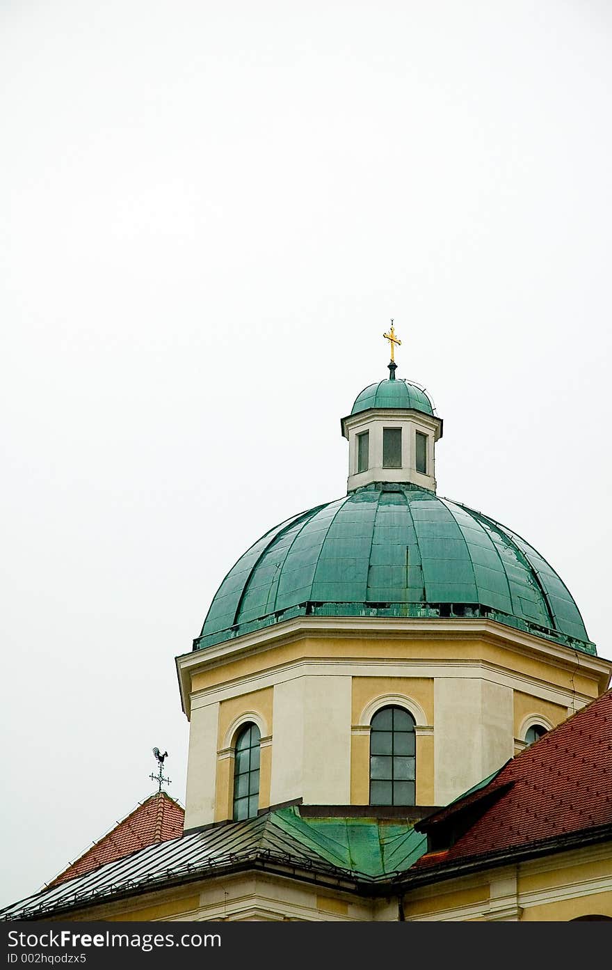 Roofs of church and house with weather vain and cross steeple