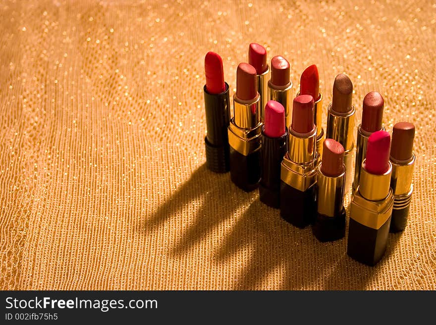 Background of gold shiny material with a dozen open tubes of lipstick. Background of gold shiny material with a dozen open tubes of lipstick.