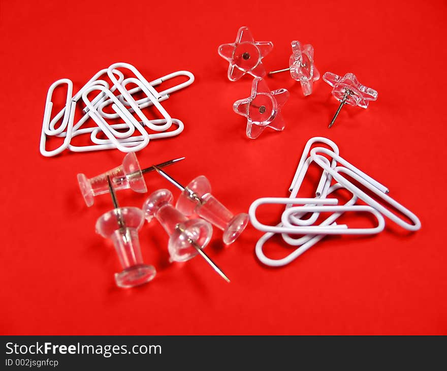 White and transparent paper clips, push pins and star shaped pins on red background. White and transparent paper clips, push pins and star shaped pins on red background