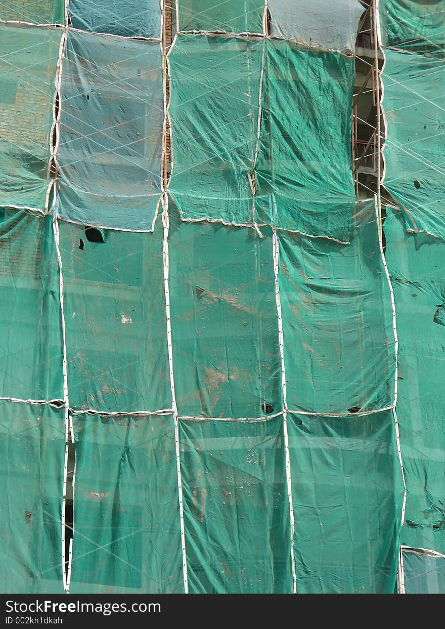 A building being constructed with scaffolding and protective netting all around, side view showing the layered colour and texture of the building, scafolding, and protective netting. A building being constructed with scaffolding and protective netting all around, side view showing the layered colour and texture of the building, scafolding, and protective netting.