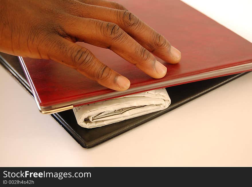 This is an image of a black hand reaching for a rolled up newspaper in between a set of portfolios. This is an image of a black hand reaching for a rolled up newspaper in between a set of portfolios.