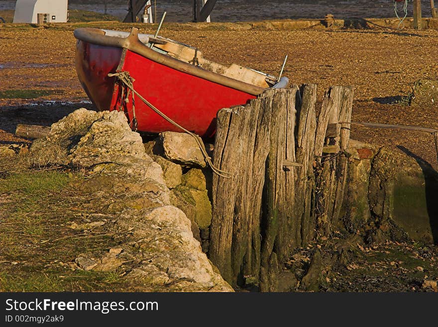 Red small rowing boat berthed on land with wooden stay. Red small rowing boat berthed on land with wooden stay.