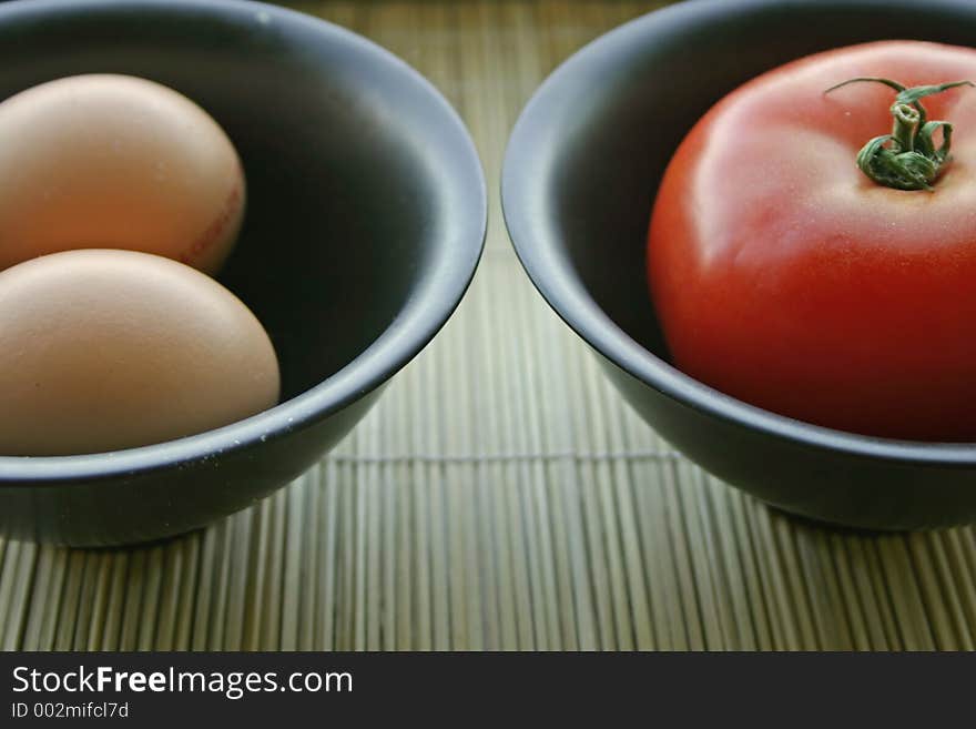 Eggs and tomatoes in black bowls. Eggs and tomatoes in black bowls